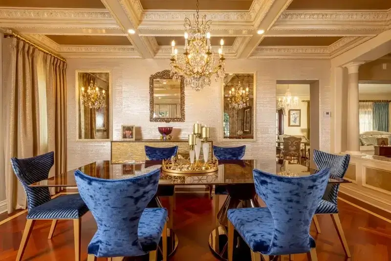 Velvet blue dining chairs, an elegant chandelier, and classic interiors for a luxurious dining room design.