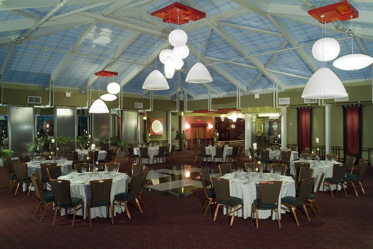 Elegant tea house banquet room with round tables, candlelit settings, and modern pendant lighting under a glass ceiling.