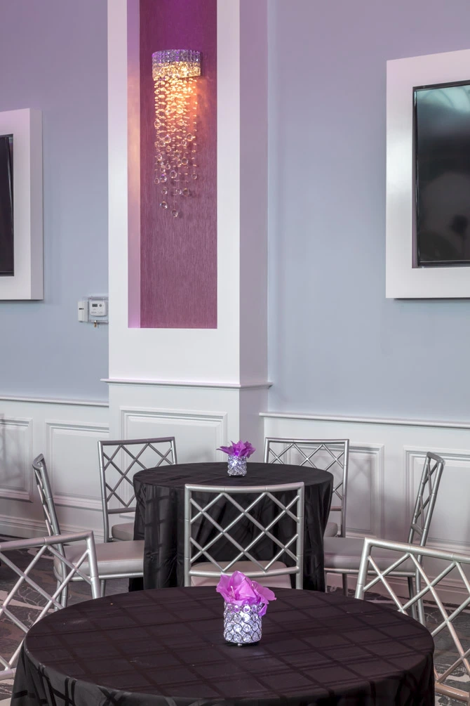 Crystal wall sconce on a purple accent wall, complemented by silver chairs for a sophisticated touch.
