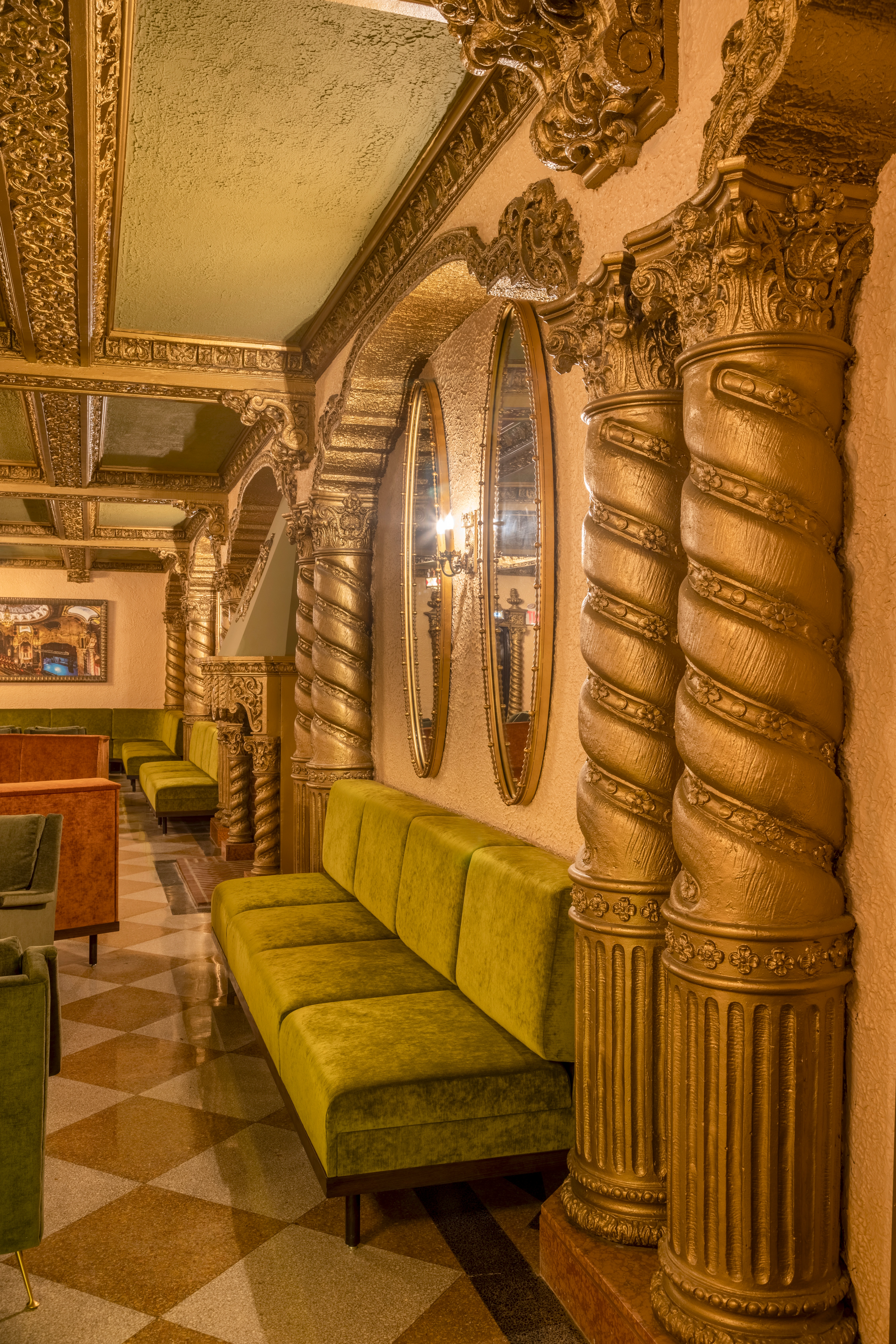 Early 1900s parlor with green velvet seating, gilded columns, ornate mirrors, terrazzo flooring, and a luxurious pre-show lounge ambiance.