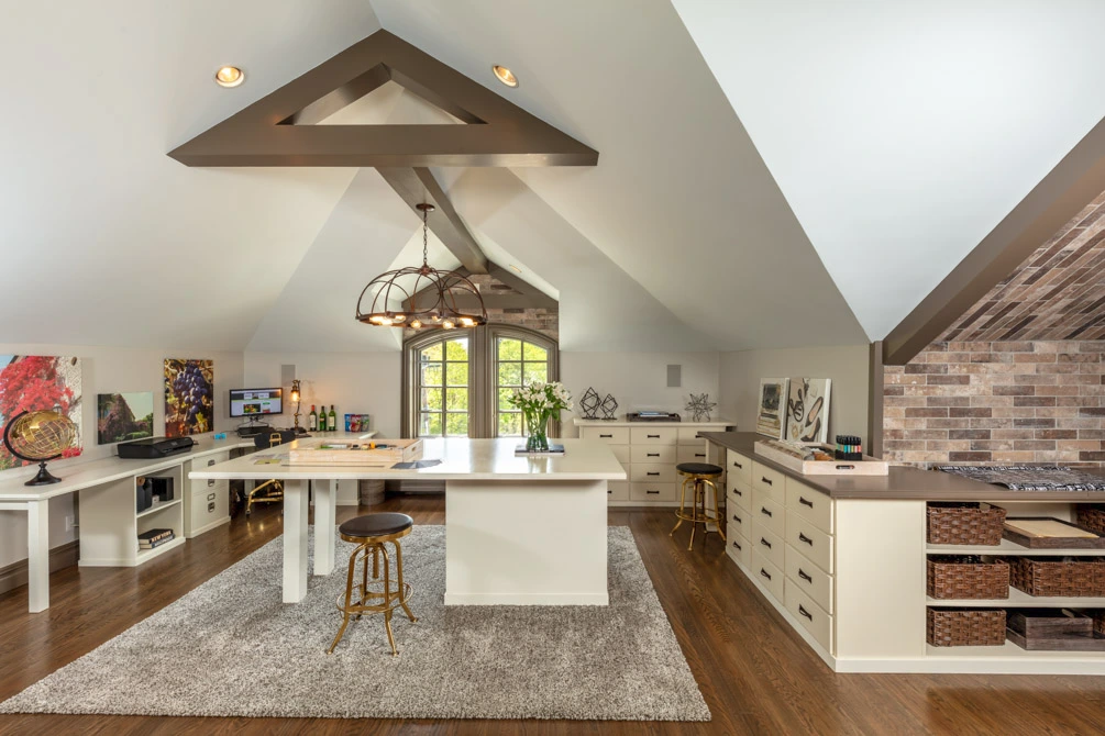 Modern rustic workspace with vaulted ceilings, a central worktable, brick accent wall, and custom cabinetry.