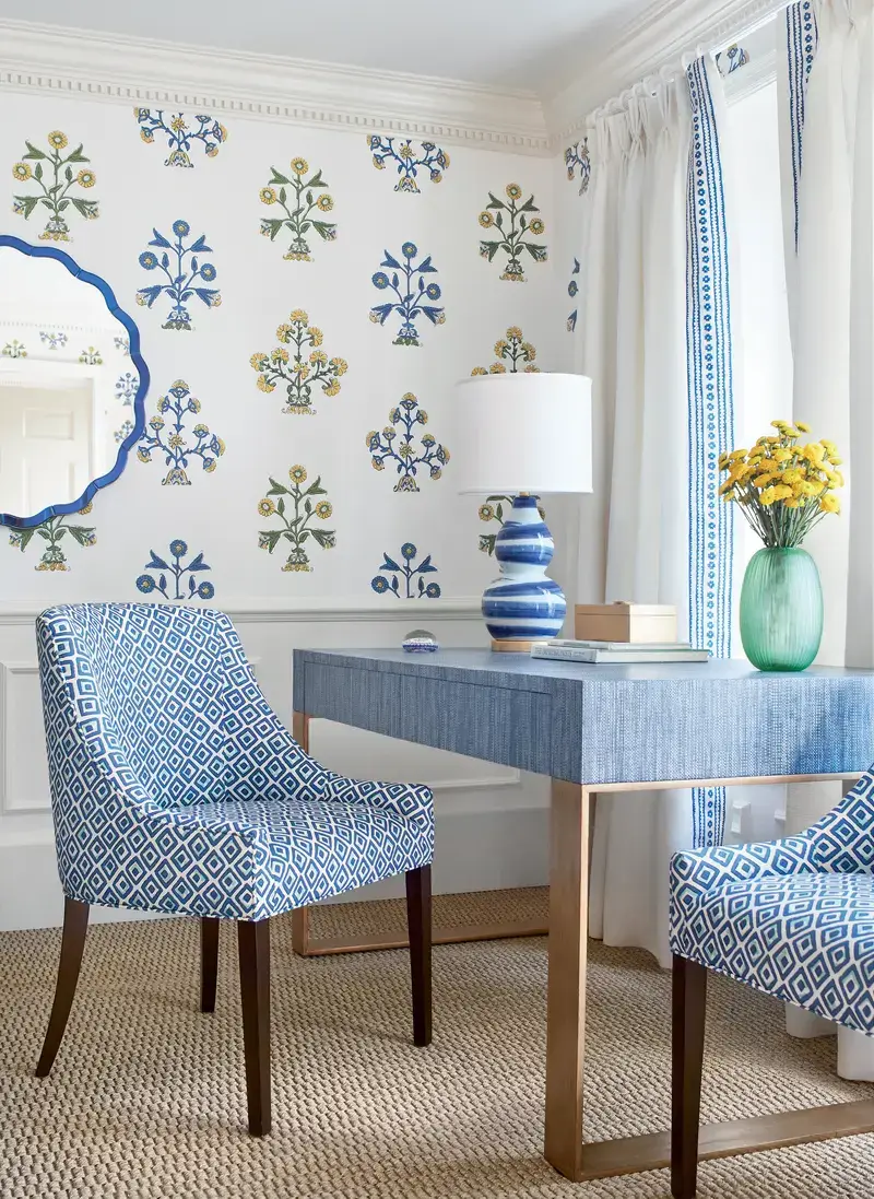 Custom neutral fabric sofa with bold geometric pillows, brass-legged desk, and patterned blue and white drapery with decorative tape.