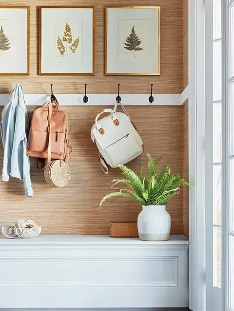 A blend of natural textures, such as a grasscloth wall treatment, framed botanical prints, and wood accents, brings warmth and charm to this welcoming entryway seating area.